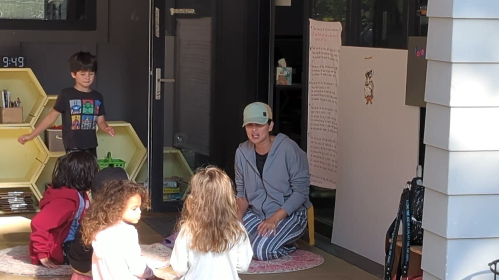 A small group sitting in a circle on the floor with a facilitator, by the hexagon cubbies
