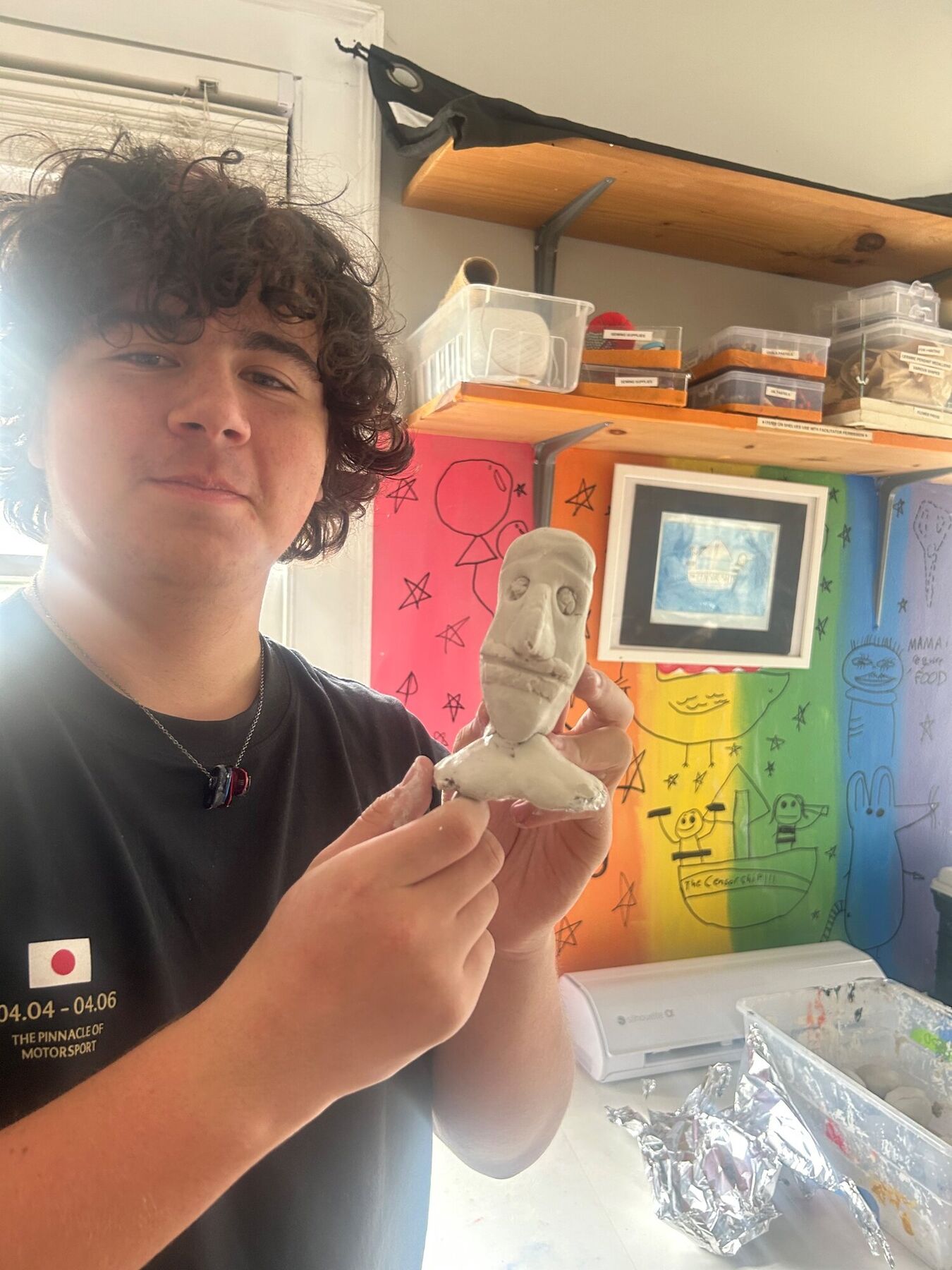 A teen holding up the clay bust he sculpted