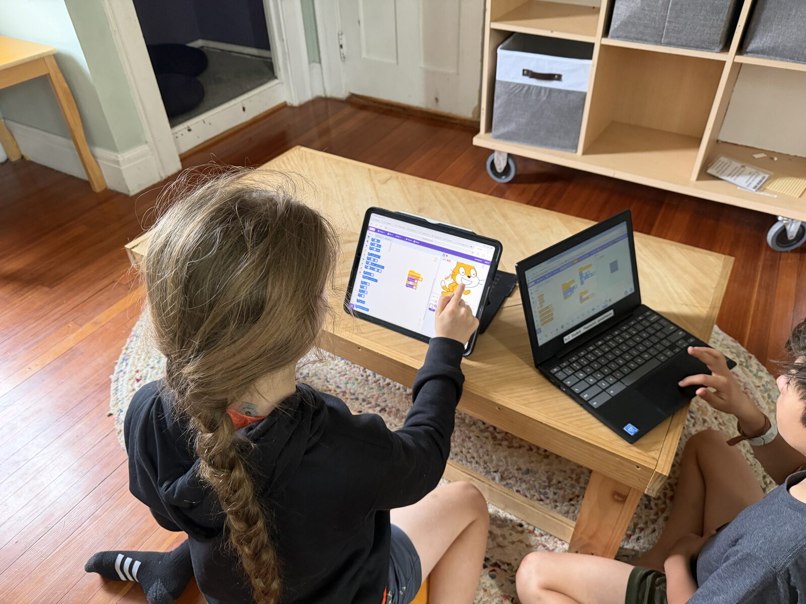 Kids coding on a tablet and a laptop around a low table
