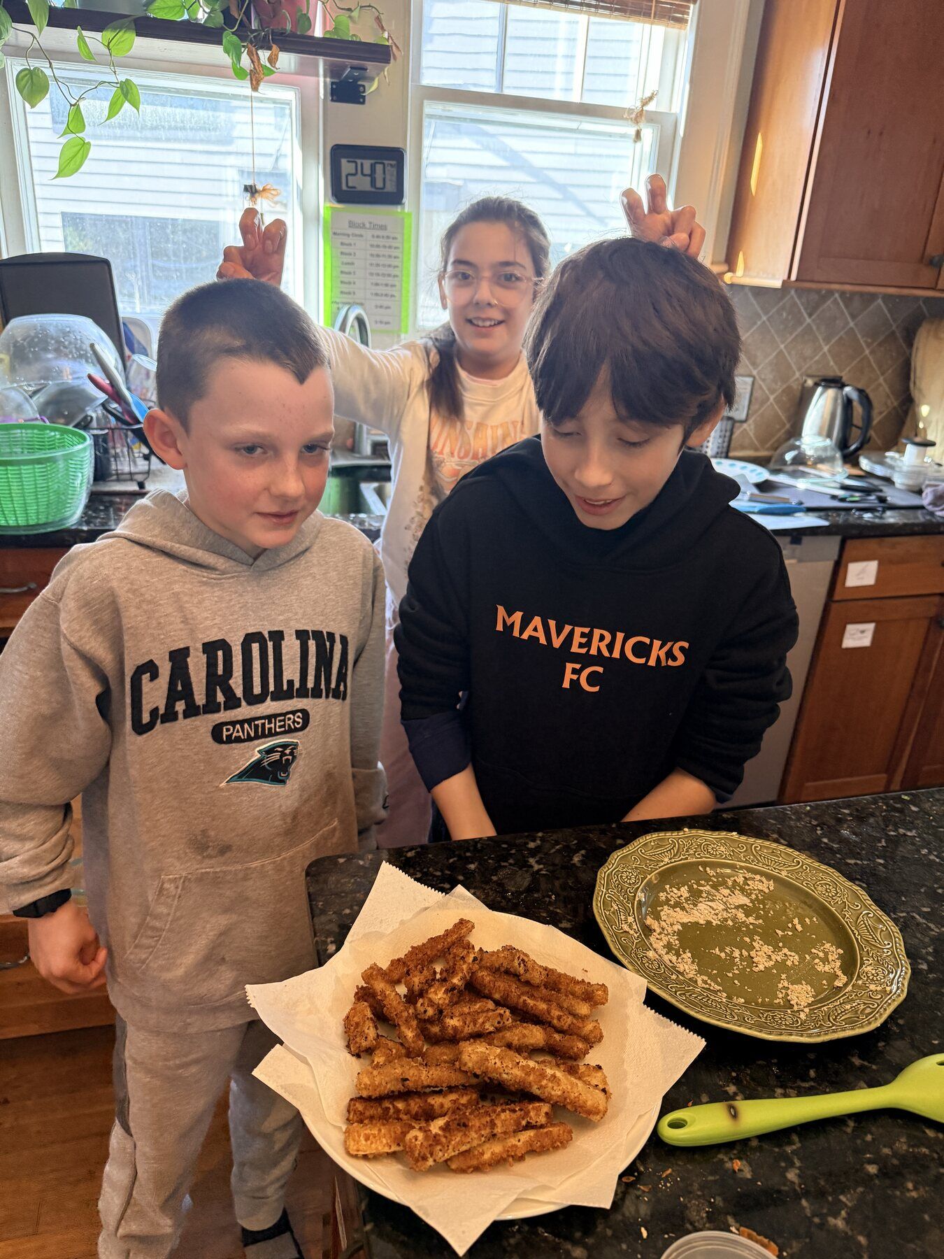 Kids proudly showing off a plate of homemade fried zucchini in the kitchen