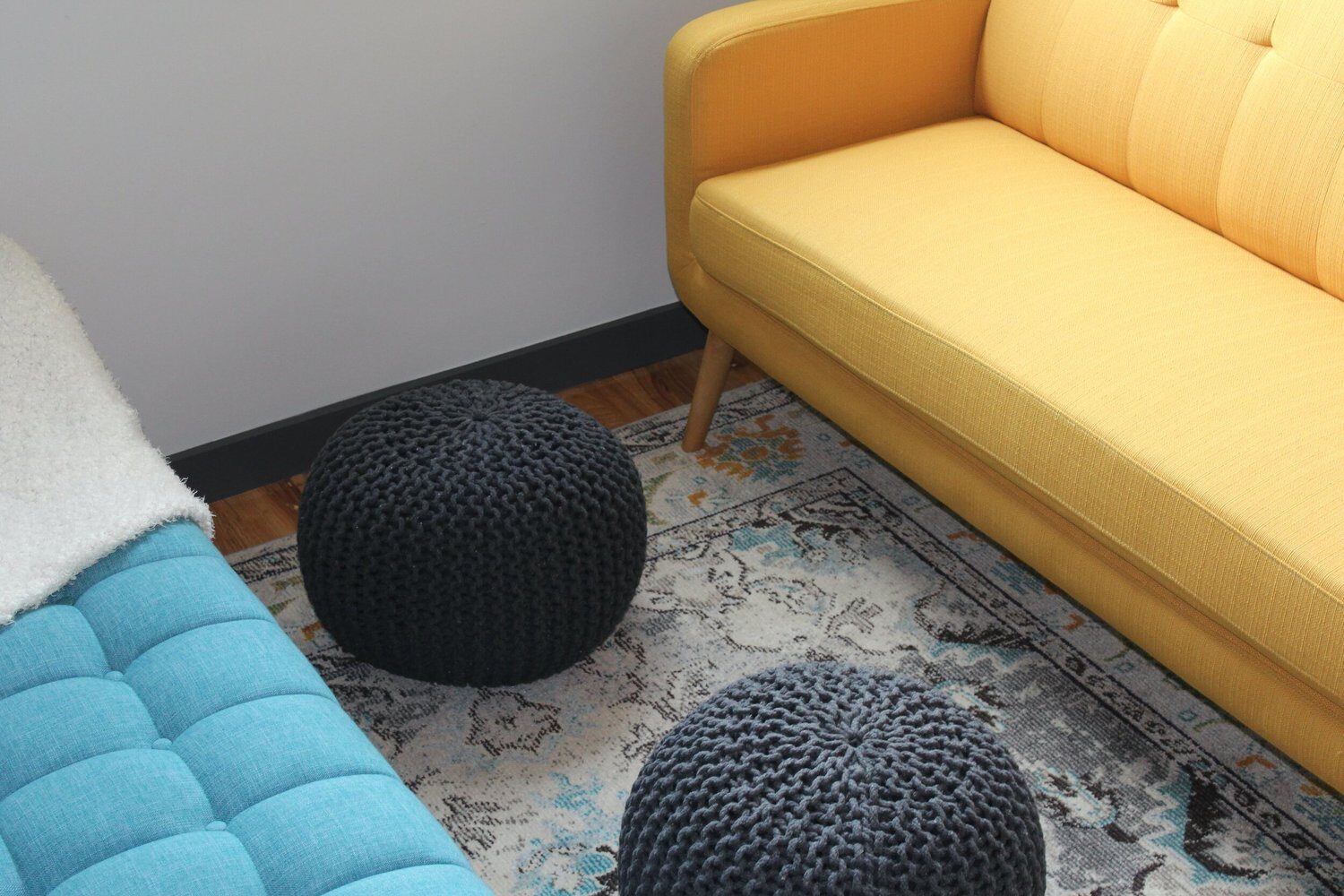 A lounge with a yellow sofa, a blue couch and knitted poufs