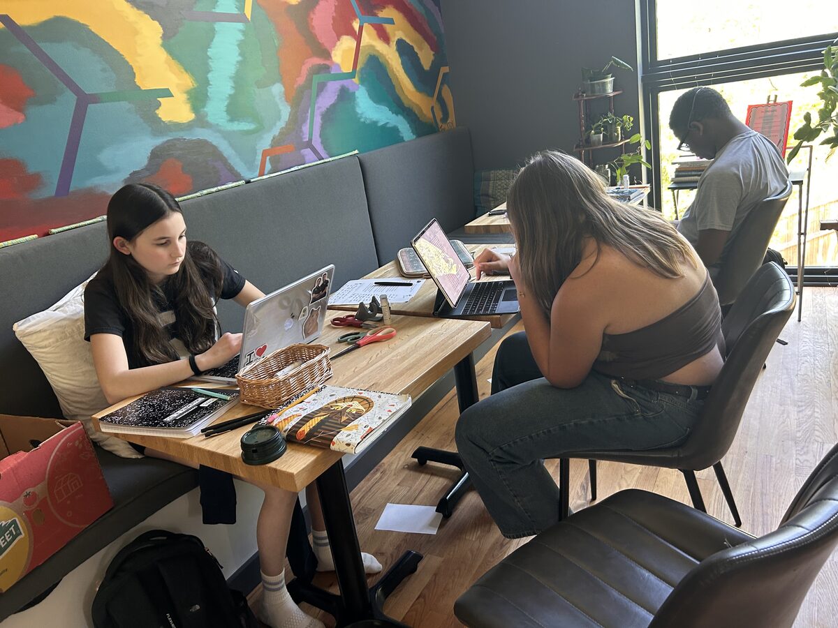 Teens working on laptops around a table at a coworking space