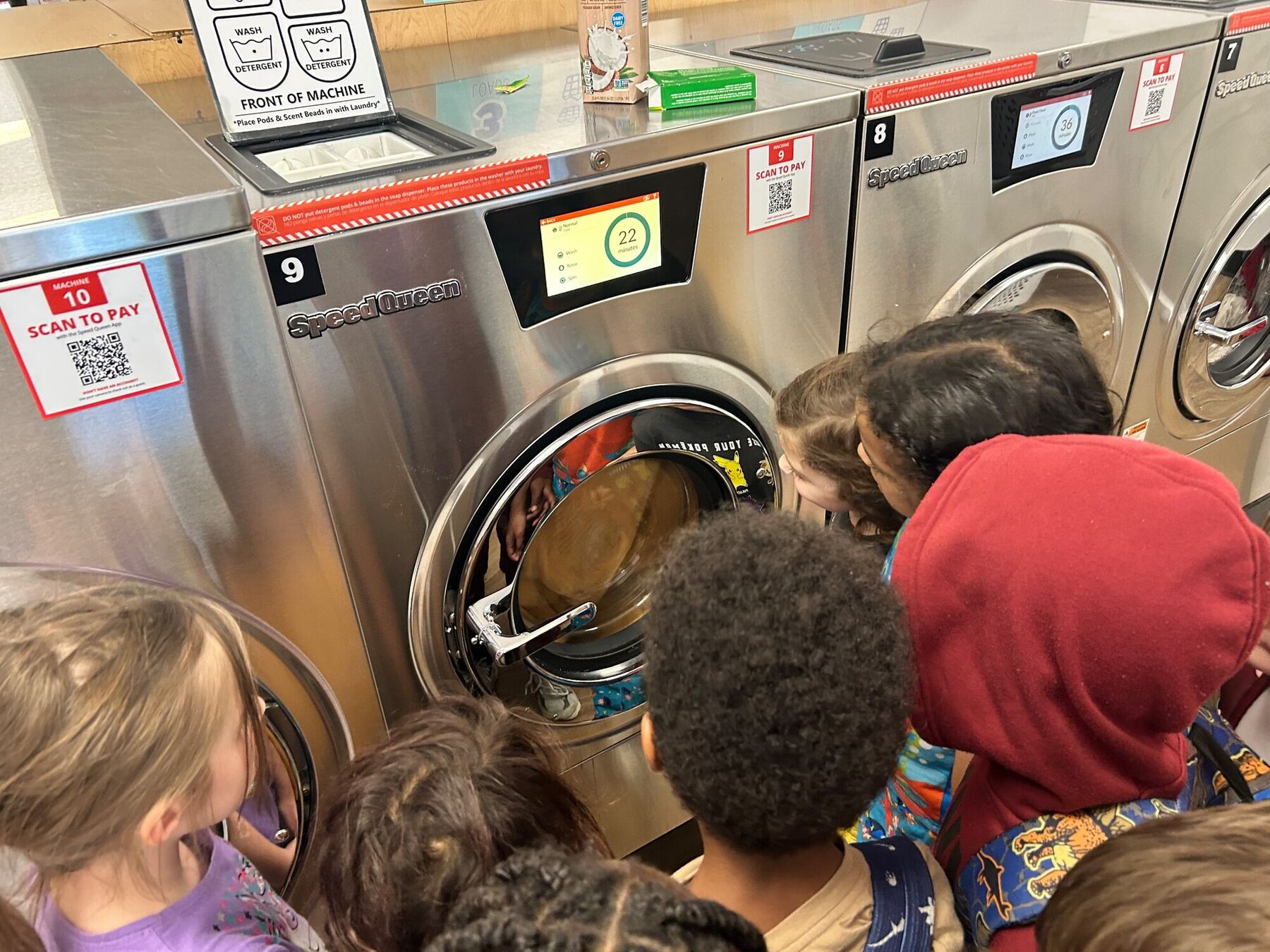 Kids crowding round the washers on a field trip to a laundromat
