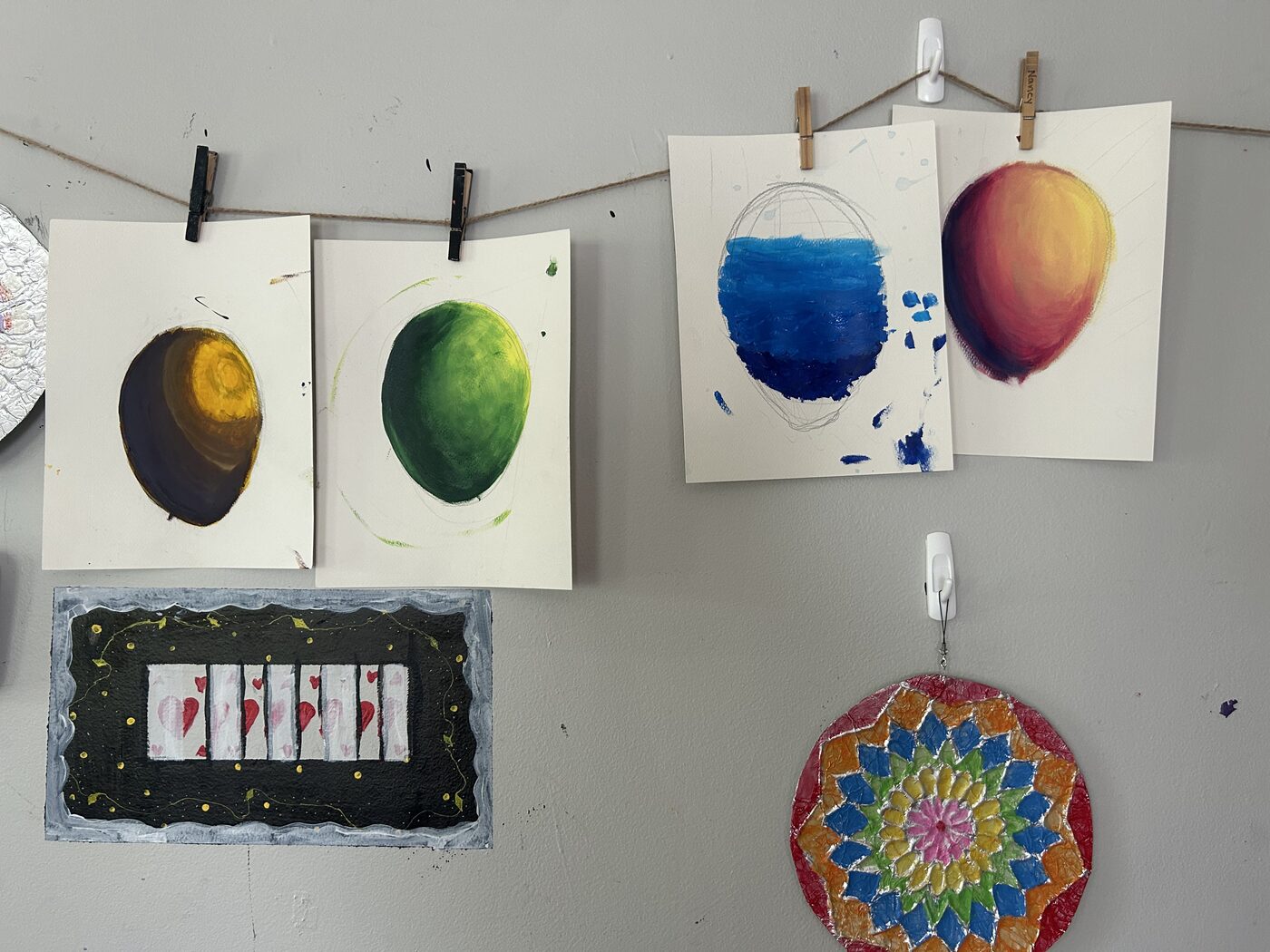 Paintings of fruit and a mandala hung up to dry on a line