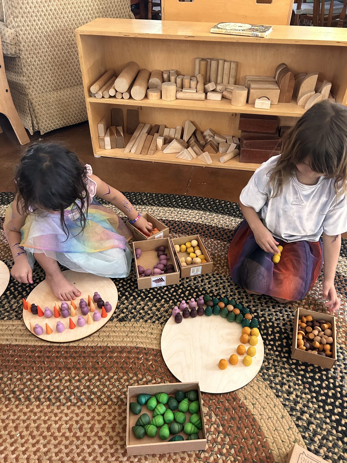 Two young kids sorting wooden pieces and felt balls on the playroom rug