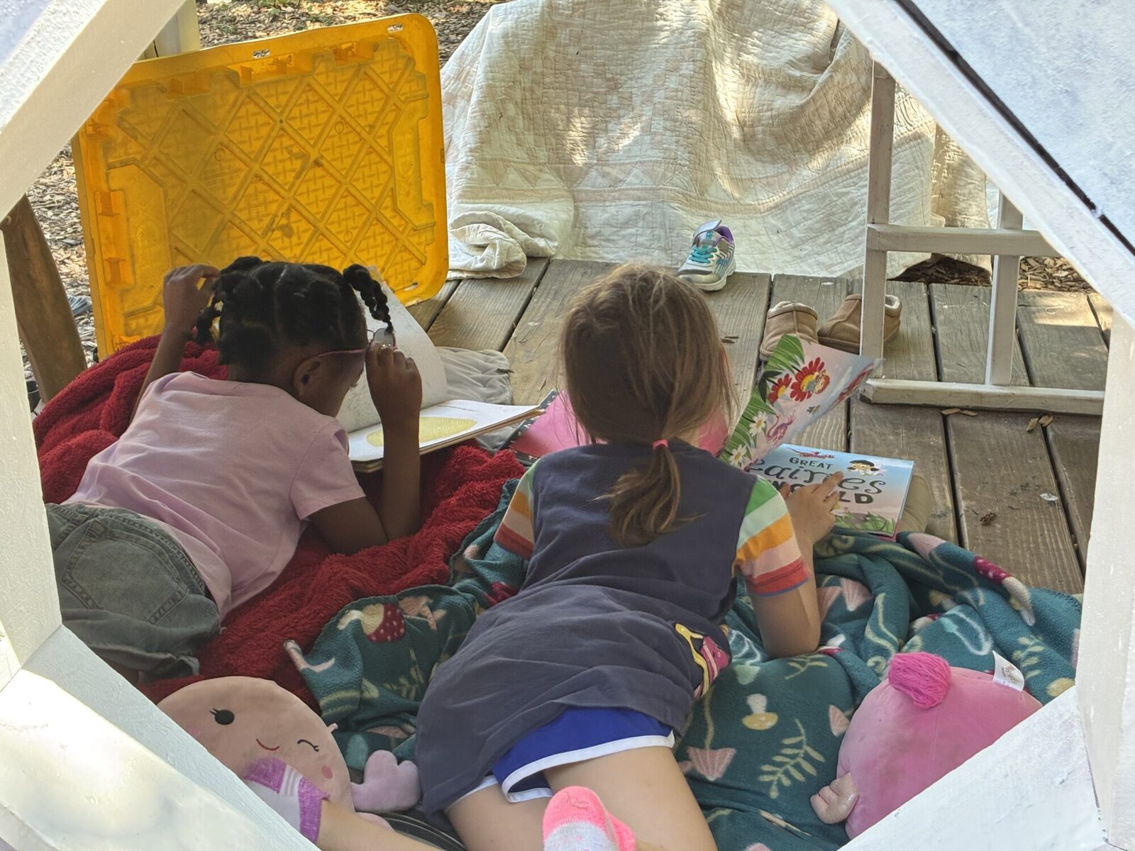 Two kids lying on blankets on the deck, reading picture books
