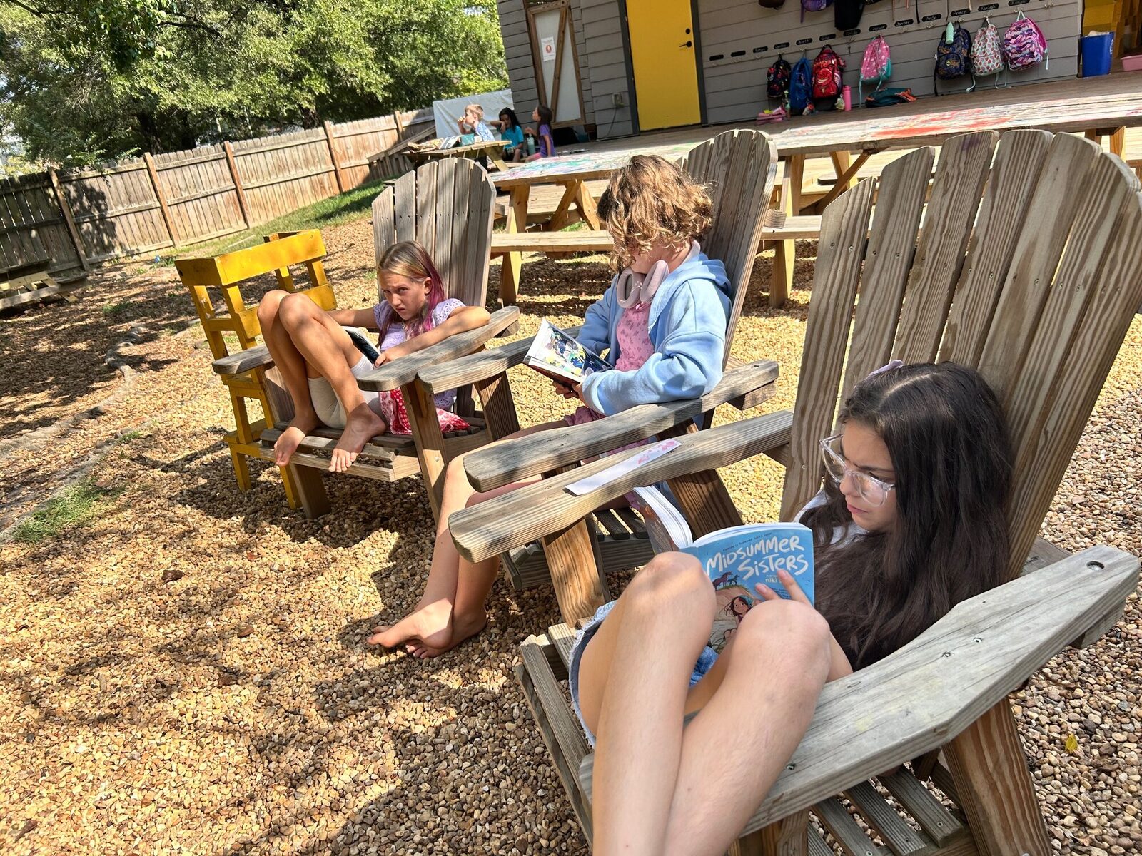 Kids reading in wooden chairs outside
